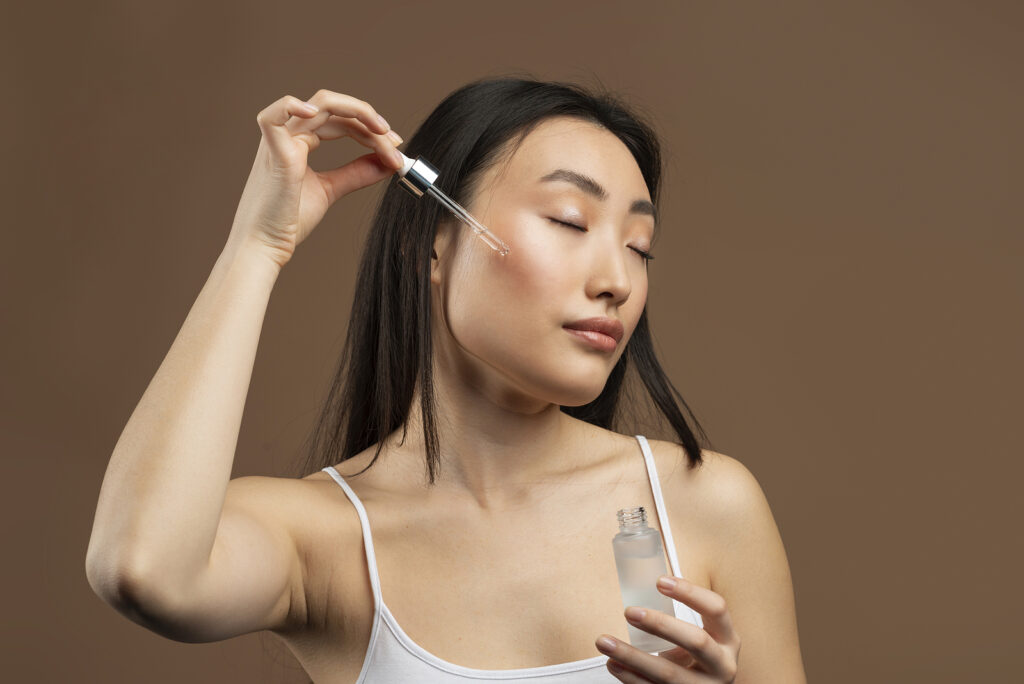 Beautiful Asian Woman Applying Face Serum With Dropper, Enjoying